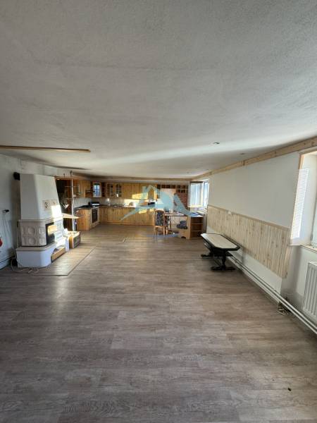 Innenraum eines Einfamilienhauses mit Küchenzeile, gemauertem Ofen und Boden in Holzoptik.