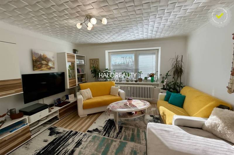 Wohnzimmer in einer Zweizimmerwohnung mit Holzboden, gelbem Sofa und Dekorationen.