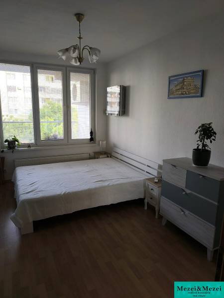 Schlafzimmer in einer 2-Zimmer-Wohnung mit Holzboden und großen Fenstern.