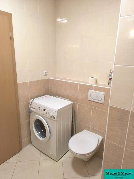 Badezimmer in einer 2-Zimmer-Wohnung mit hellen Fliesen, Waschmaschine und hängendem WC.