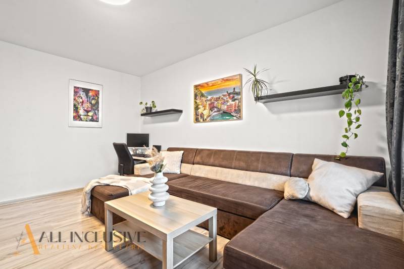 Wohnzimmer mit braunem Sofa, Schreibtisch und Boden in Holzoptik.