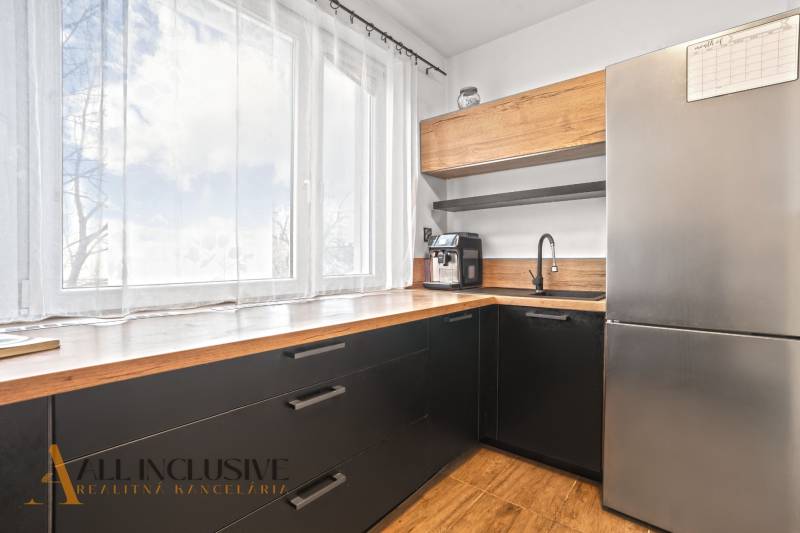 Küche in einer 3-Zimmer-Wohnung mit großem Fenster, schwarzen Schränken und Boden mit Holzdekor.