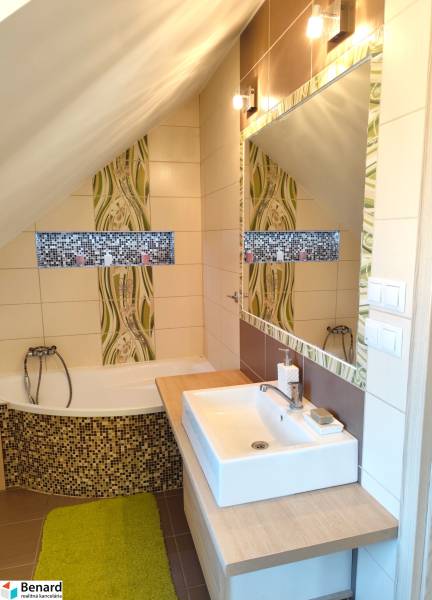 Ein Badezimmer in einem Einfamilienhaus mit einer Badewanne, einem Waschbecken, einem Spiegel und Mosaikdekoration.