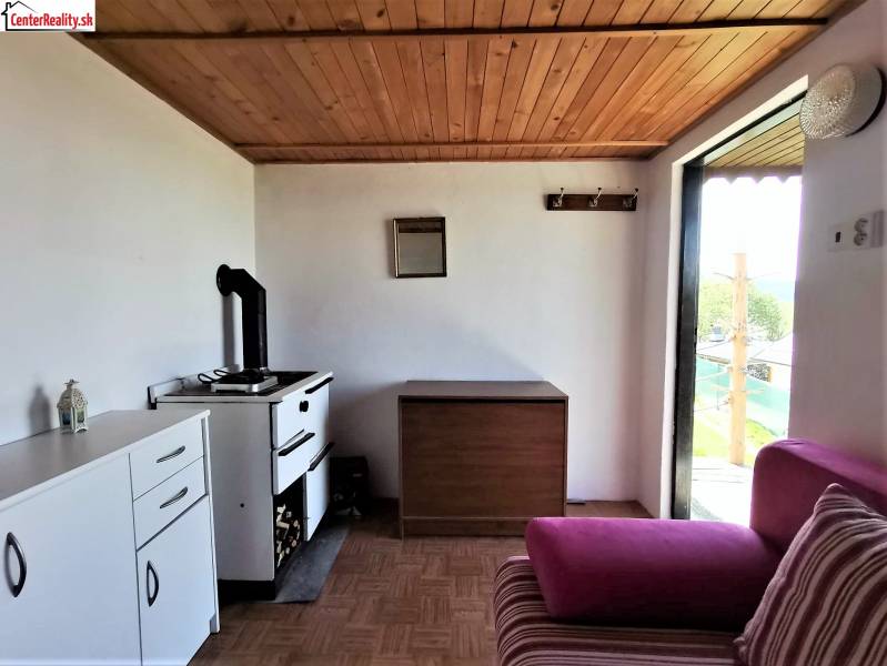 In der Chatküche gibt es einen Ofen, einen Schrank, ein rosa Sofa und einen Blick auf den Garten.