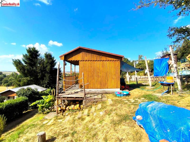 Eine Holzhütte in Partizánske, umgeben von Natur, mit einem grasbewachsenen Grundstück und einer Außensitzgelegenheit.