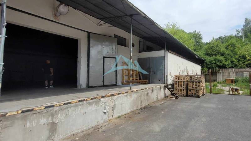 Lagerhallen und Schuppen in der Eisenbahnstraße mit Paletten und Unterstand, daneben sind Büsche.