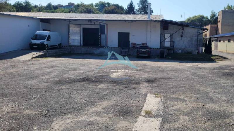 An der Straße Železničná befinden sich Lager und Hallen, ein Bereich mit Parkplätzen und Autos.