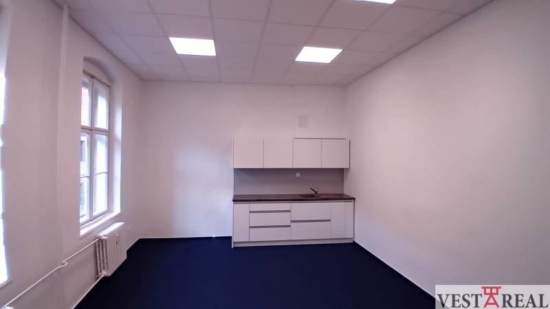 Büros mit Küchenzeile und blauem Teppich, weiße Wände und großes Fenster.