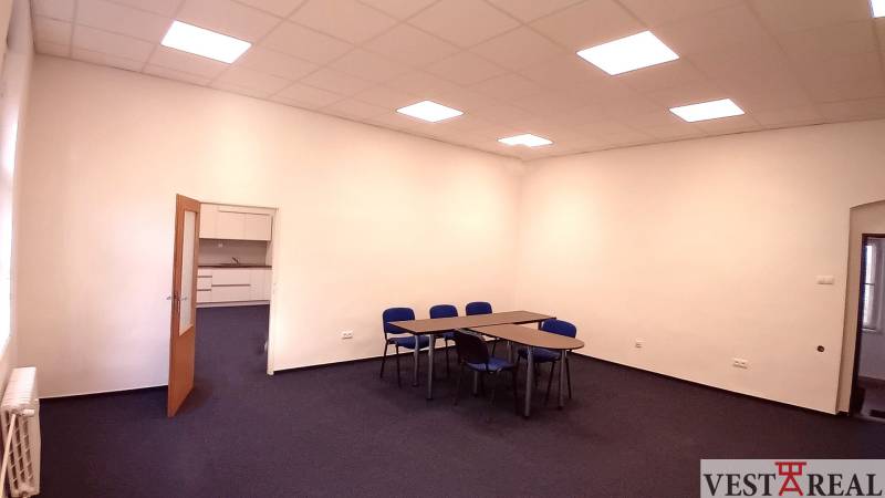 Ein Büro mit blauen Stühlen und Tischen, weiße Wand, offene Tür zu einer kleinen Küche.