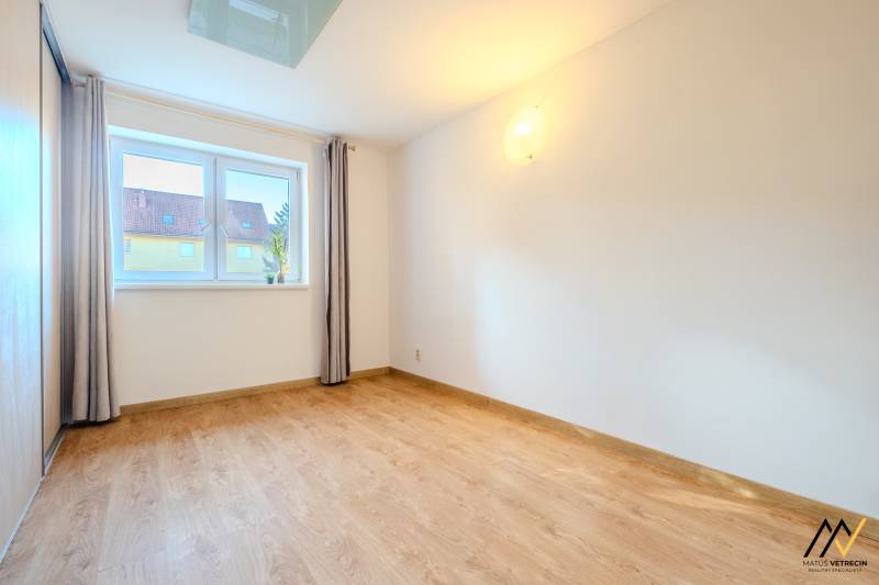 Ein heller Raum mit einem Holzboden in einer 2-Zimmer-Wohnung, Vorhänge und ein Fenster.