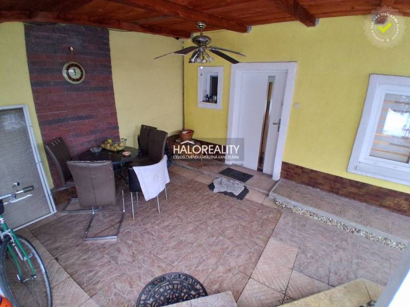 Die Terrasse des Einfamilienhauses mit Fliesen und Sitzmöbeln. In der Nische befinden sich ein Tisch und eine Uhr.