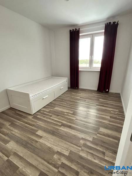 Ein Zimmer mit einem Bett, einem Boden in Holzoptik und einem großen Fenster in einer 3-Zimmer-Wohnung.