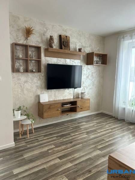 Wohnzimmer in einer 3-Zimmer-Wohnung mit Holzboden, einem aufgehängten Fernseher und Dekorationen.