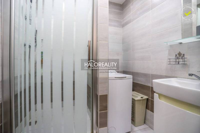 Badezimmer mit Waschmaschine und Duschkabine in einer 3-Zimmer-Wohnung, helle Fliesen, sauberes Design.