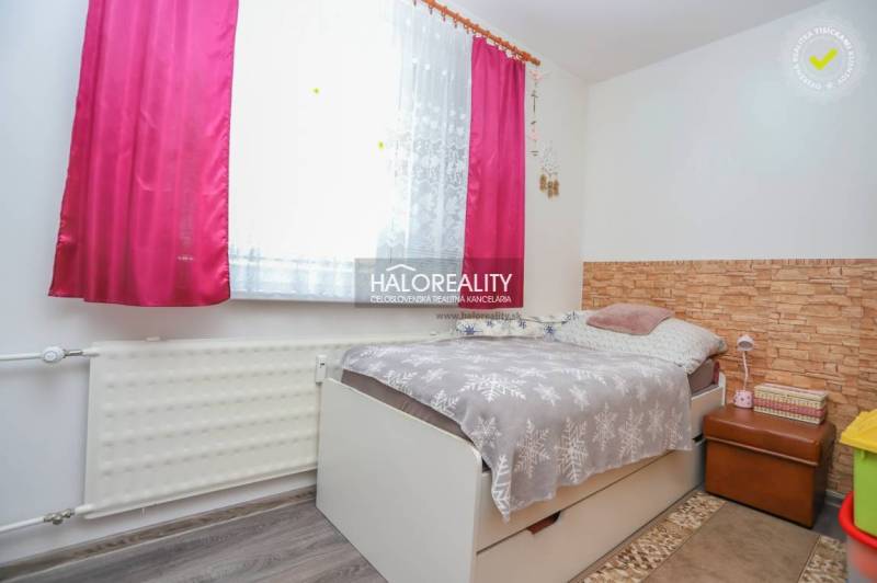 Ein Zimmer in einer 3-Zimmer-Wohnung mit einem Bett, einem Blumenvorhang und einem Boden mit Holzdekor.