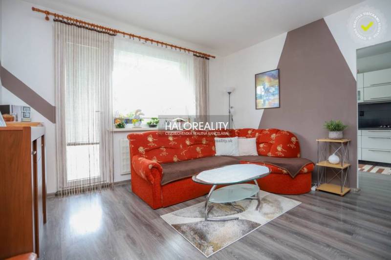 Wohnzimmer in einer 3-Zimmer-Wohnung mit einem orangefarbenen Sofa und einem Boden in Holzoptik.