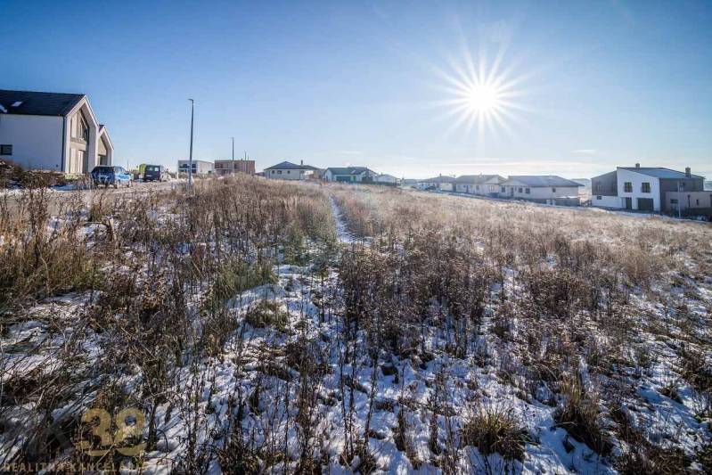 Ein verschneites Grundstück in Mlynica mit Wohnhäusern im Hintergrund, ideal zum Wohnen.