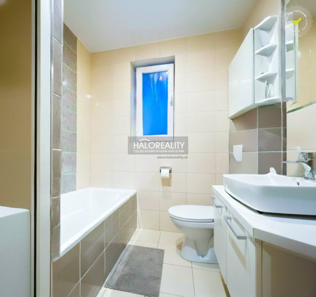 Badezimmer mit Badewanne und Waschbecken in einer 2-Zimmer-Wohnung, dominiert von hellen Fliesen.