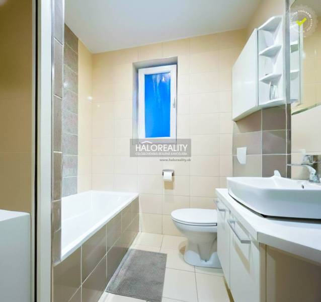 Badezimmer mit Badewanne und Waschbecken in einer 2-Zimmer-Wohnung, dominiert von hellen Fliesen.