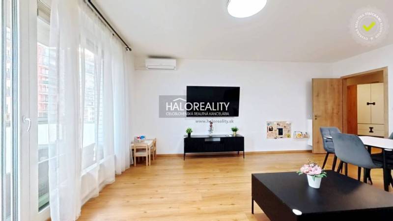 Wohnzimmer in einer Zweizimmerwohnung mit Holzboden, großem Fenster und Esstisch.