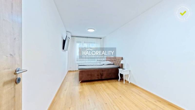 Helles Schlafzimmer mit Bett, Nachttisch und Fernseher in einer 2-Zimmer-Wohnung, Boden mit Holzdekor.