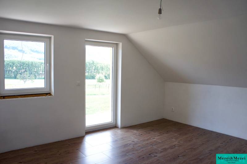 Helles Zimmer mit Fenstern, Holzboden und Glastüren in einem Einfamilienhaus.