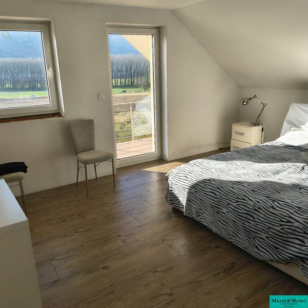 Helles Schlafzimmer in einem Einfamilienhaus mit Bett, Stuhl und Boden in Holzoptik.