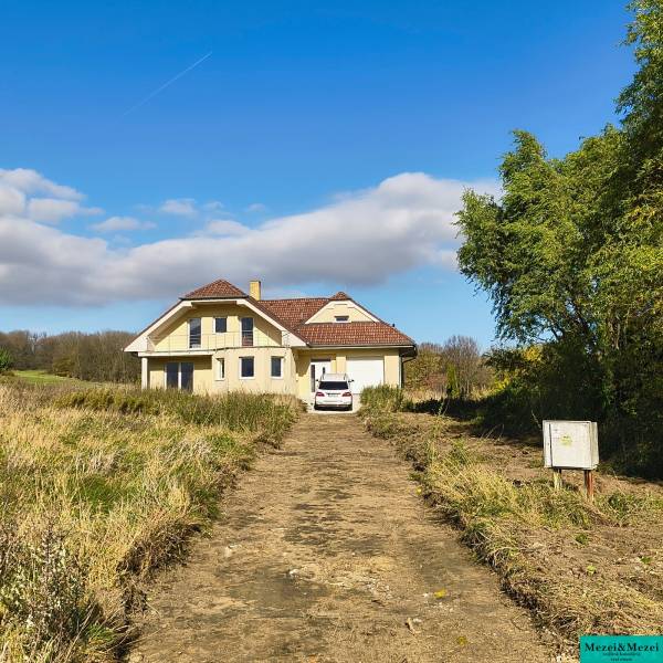 Ein Einfamilienhaus in Buková mit Zufahrtsstraße, Auto und umliegender Natur unter blauem Himmel.