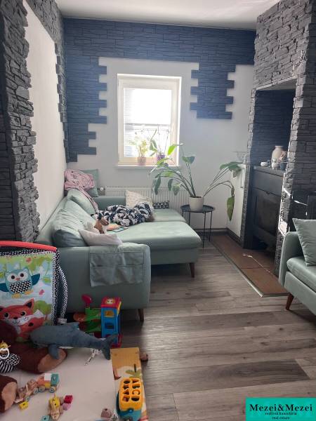 Wohnzimmer mit grünem Sofa, Spielzeug, Pflanzen und Wänden mit Steinverkleidung in einer 4-Zimmer-Wohnung.