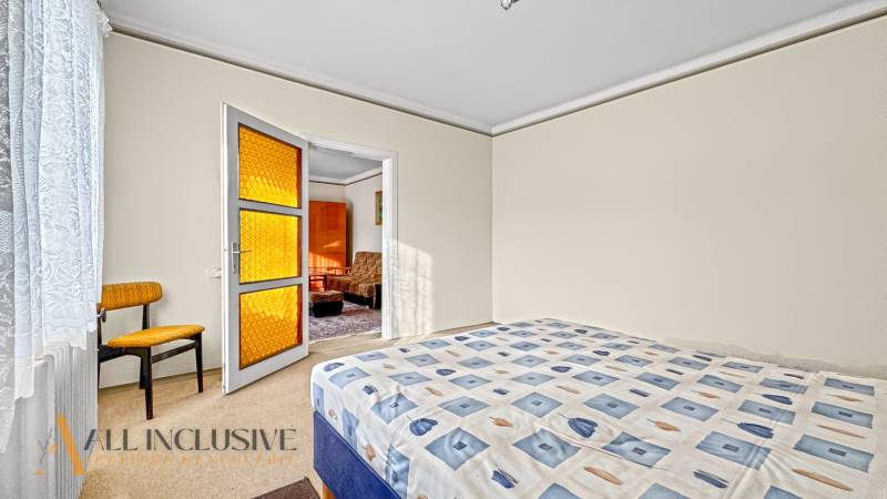 Schlafzimmer im Einfamilienhaus mit Bett, Sessel und Tür mit orangefarbenem Glas.