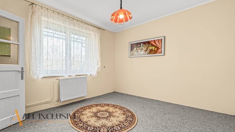 Ein Zimmer in einem Einfamilienhaus mit einem hellen Teppich, Vorhängen und einem Wandbild.
