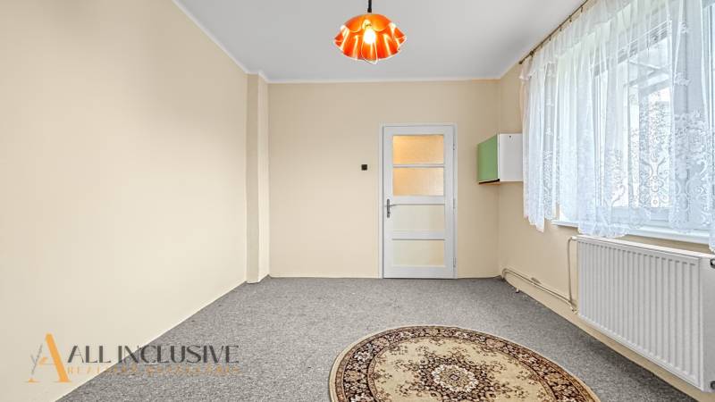 Ein helles Zimmer in einem Einfamilienhaus mit Teppichboden und einem Fenster mit Spitzenvorhang.