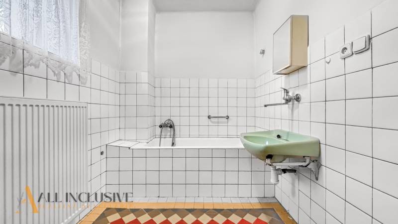 Ein Badezimmer in einem Einfamilienhaus mit einer rechteckigen Badewanne, einem grünen Waschbecken und auffälligen Fliesen.