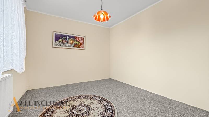 Ein Zimmer in einem Einfamilienhaus mit Teppich, Vorhang, Bild und einer Deckenleuchte.