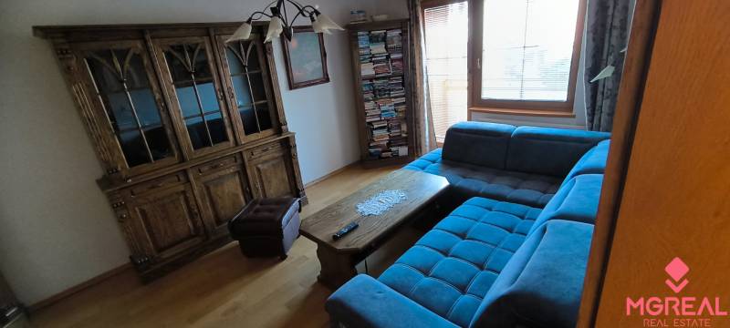 Wohnzimmer mit blauem Sofa, Holzkommode und Boden in Holzoptik.