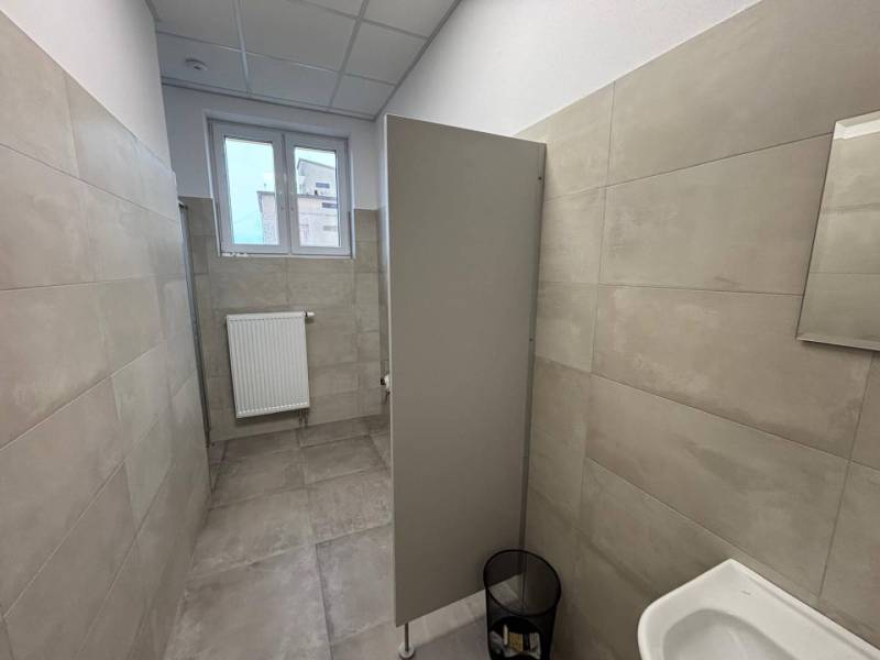 Büros mit grauer Verkleidung und Toilette, mit kleinem Fenster und Rippenheizkörper.