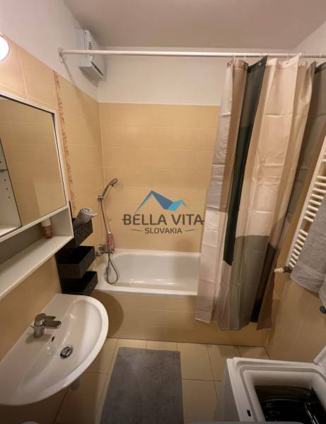 Badezimmer in einer 2-Zimmer-Wohnung mit Badewanne, Waschbecken, Waschmaschine und Fliesen.