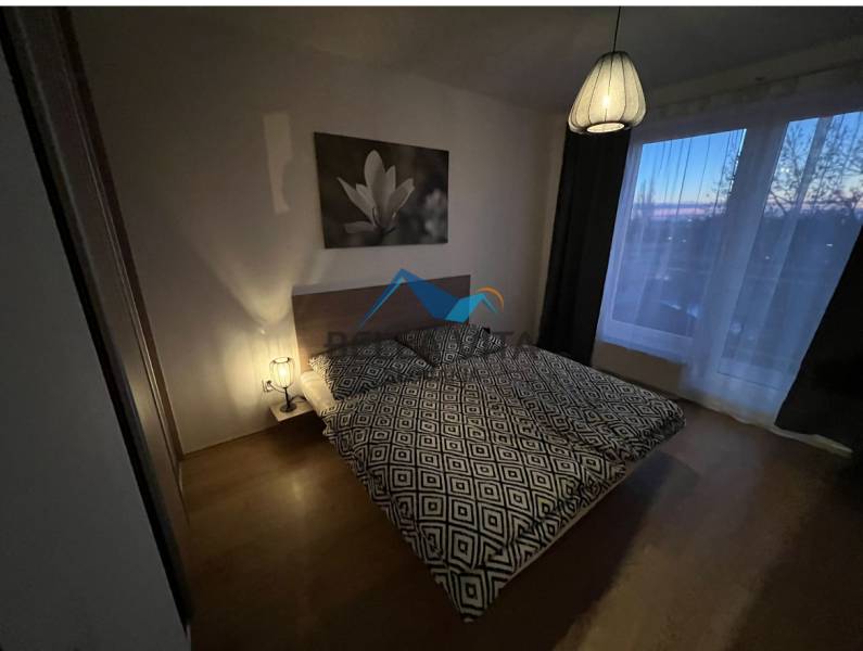 Schlafzimmer in einer 2-Zimmer-Wohnung mit Bett, Lampe, Bild und Boden mit Holzdekor.
