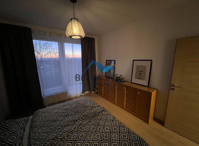 Schlafzimmer mit Kommode und Lampe, Boden mit Holzdekor in einer 2-Zimmer-Wohnung.