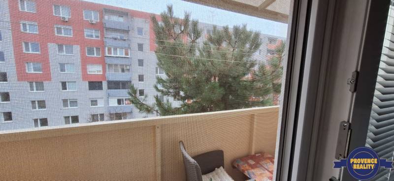 Der Balkon einer 2-Zimmer-Wohnung in Komárno mit Blick auf ein Plattenbau und einen Baum.