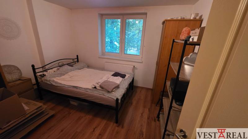 Schlafzimmer in einer 3-Zimmer-Wohnung mit einem Metallbett und einem Boden in Holzoptik.