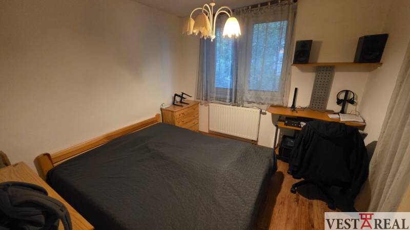 Schlafzimmer in einer 3-Zimmer-Wohnung mit Bett, Schreibtisch und Boden mit Holzdekor.