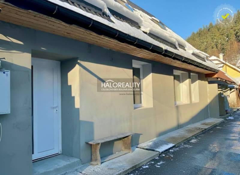 Ein Einfamilienhaus in Hronec mit Schnee auf dem Dach, einer weißen Tür und einer Holzbank.