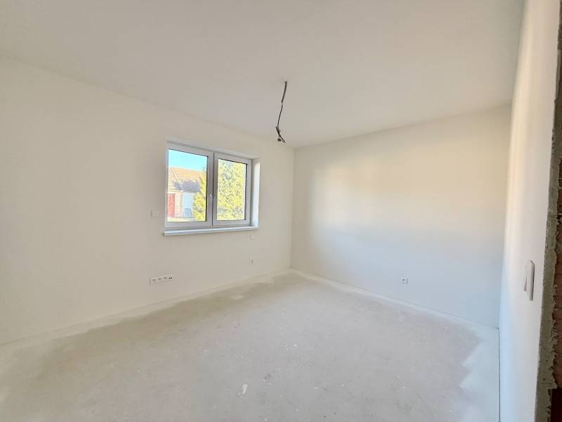 Ein geräumiges, helles Zimmer in einem Einfamilienhaus mit Doppelfenster und weißen Wänden.