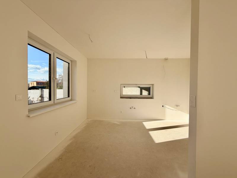 Innenraum eines Einfamilienhauses ohne Bodenbelag und mit Fenstern auf der Sonnenseite.