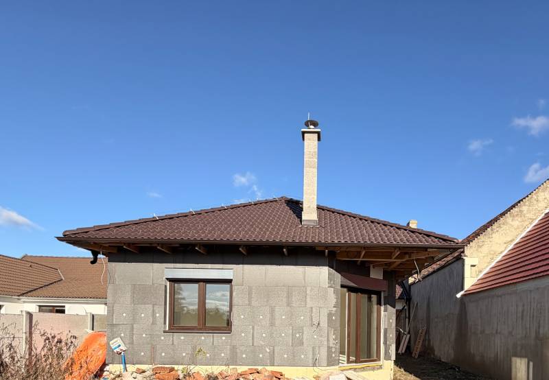 Ein Einfamilienhaus im Bau in Cífer mit einem braunen Dach und einem Schornstein.