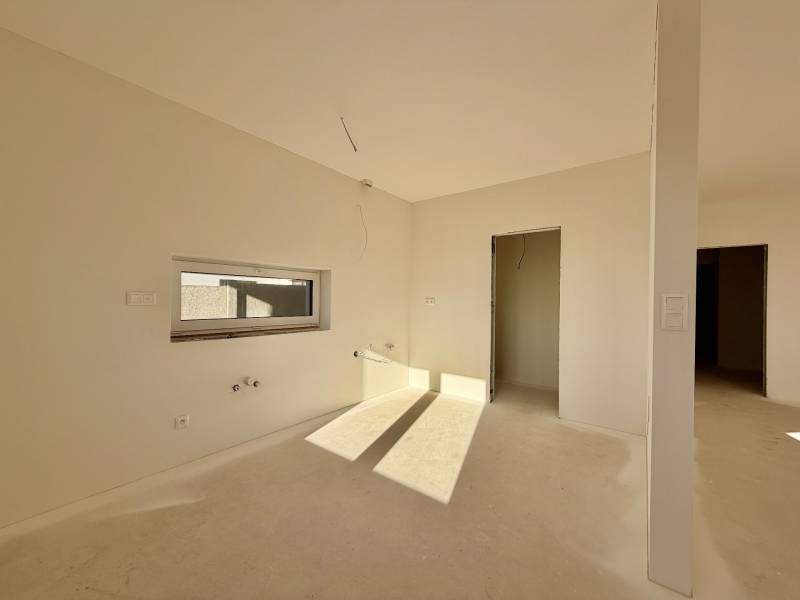 Ein geräumiger, unmöblierter Raum in einem Einfamilienhaus mit einem Fenster und einer Tür ohne Boden.