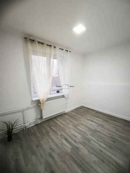 Ein Zimmer in einer 4-Zimmer-Wohnung mit einem Boden in Holzoptik, Vorhängen und einem Heizkörper.