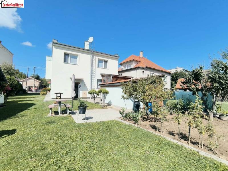 Ein Einfamilienhaus in Partizánske, umgeben von einem grünen Rasen und einem Garten unter blauem Himmel.