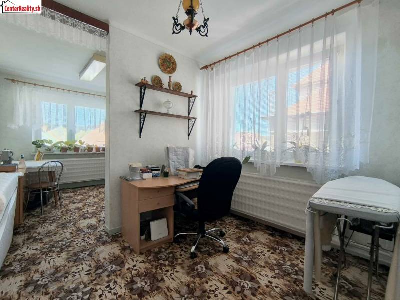 Ein Zimmer in einem Einfamilienhaus mit einem Schreibtisch, Pflanzen und einem Teppich mit Blumenmuster.